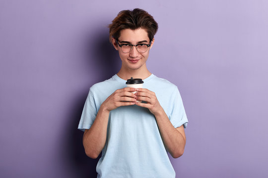 cute young stundent holding coffee and posing to the camera. leisure, breakfast. close up portrait. isolated blue background