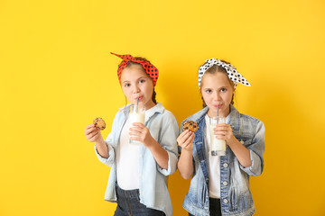 Portrait of cute twin girls with cookies and glasses of milk on color background