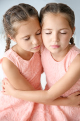 Portrait of cute twin girls on light background