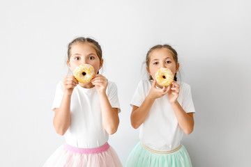 Portrait of cute twin girls with tasty donuts on light background