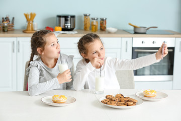 Portrait of cute twin girls with milk taking selfie in kitchen