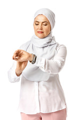 Beautiful mature Muslim woman looking on her wrist watch on white background