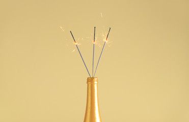 Bottle of champagne with festive Christmas sparklers on color background