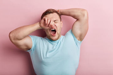 Sleepy young muscular strong man yawning, he rubs his eye in the morning, close up portrait,...