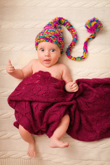 Close portrait of adorable baby in knitted funny gnome hat lies on his back.