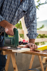 Adult craftsman carpenter with electric saw working on cutting a wooden table. Housework do it yourself. Stock photography.