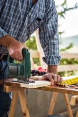 Adult craftsman carpenter with electric saw working on cutting a wooden table. Housework do it yourself. Stock photography.