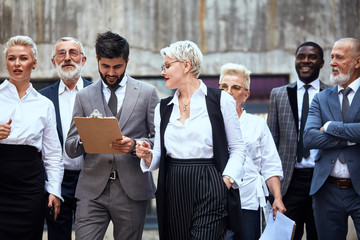 Six caucasian and one african businessmen dressed in stylish office clothes move in street. Woman...