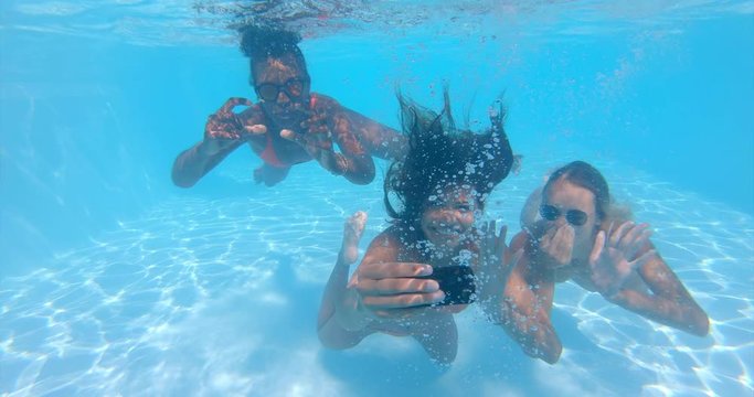 Underwater shot of young multi-ethnic girlfriends in swimwear are having fun to enjoy their summer vacation and making selfie in swimming pool in a sunny day.