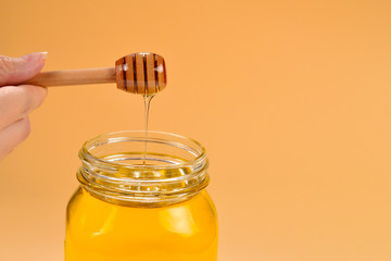 Dipper with honey in woman hand on orange background. Space for text or design.