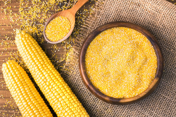 Corn grits in a wooden bowl on the background of fresh corn on the cob on a burlap.