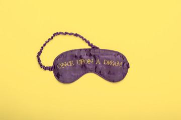 Purple satin  sleeping mask on yellow background. Mininal flat lay concept.