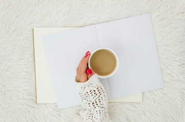 Top view female hand with coffee cup on a opened blank magazine. Still life concpept