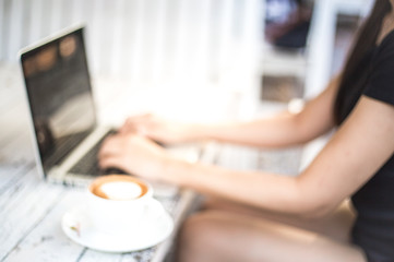 Blurred background of a woman working on laptop with coffee on desk