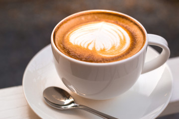 A cup of a latte art coffee with spoon on white table