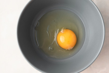 Raw uncooked egg in gray bowl, top view. Yellow egg yolk and liquid egg whites. Ingredient for baking, scrambled eggs or omelet