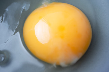 Close-up raw uncooked egg in gray bowl, top view. Macro yellow egg yolk and liquid egg whites with selective focus. Ingredient for baking, scrambled eggs or omelet