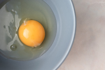 Close-up raw uncooked egg in gray bowl with copy space, top view. Yellow egg yolk and liquid egg whites. Ingredient for baking, scrambled eggs or omelet