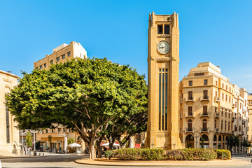 Fototapeta premium Wieża zegarowa na placu Al-Abed Nejmeh z drzewami i budynkami dookoła, Bejrut, Liban