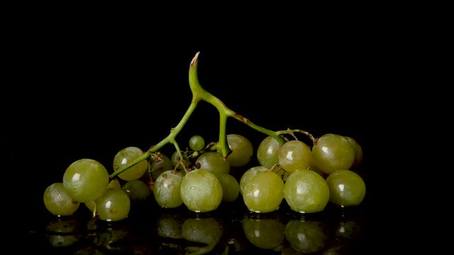 A static slow motion footage under controlled studio lighting,showing bunch of grapes falling on a table with water splashing ,isolated on a black background. A close up view.