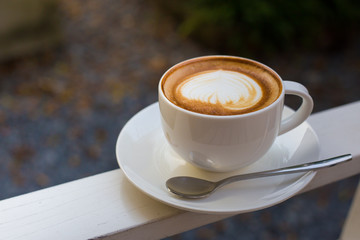 A cup of a latte art coffee with spoon on white table