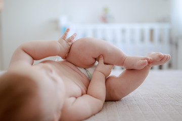 Adorable Caucasian playful baby boy in diaper lying on bed and trying to reach foot.
