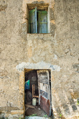 Tinkered door and tired shutters on an old dilapidated house with decrepit walls