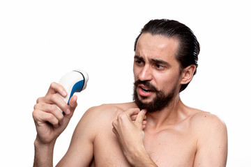 Handsome bearded man with mustache looks at the electric razor standning bare isolated over white...