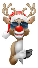 Christmas reindeer red nosed deer cartoon character wearing cool shades or sunglasses and a Santa hat peeking around a sign and pointing at it