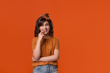 Smiling brunette woman in a t-shirt and beautiful headband standing isolated over orange background. Place for ad.