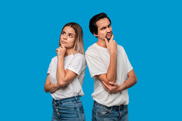 Fototapeta premium Thoughtful couple of a bearded brunet man with mustache and blond woman in white t-shirts and blue jeands standing isolated over white background.