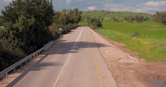 Drone fly over the highway in a rural area green akk over and blue sky with cars passing by