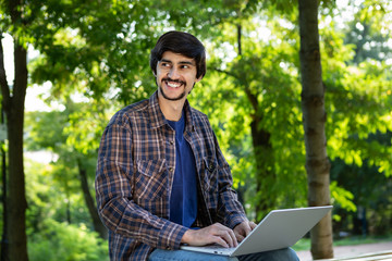 Young bearded brunet freelancer with mustache sitting with a laptop in a park. Work anywhere