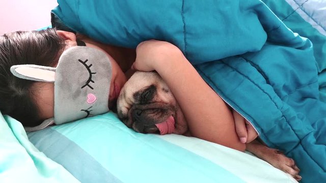 Young woman wear eyes mask is lying down and sleeping rest with pug dog puppy in bed. Nap with hugging dog