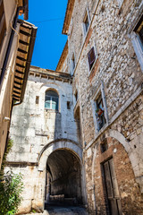 Fototapeta na wymiar A characteristic glimpse of the city of Amelia, in Umbria. The cobbled alley, the stone and brick walls of the old houses in the historic center. A small gallery with arch.