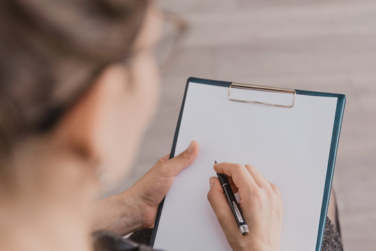 the woman holds a pen and writes in a notebook. Close-up, top view A woman's hand writes in a blank white sheet, tablet, not to forget or make a list of plans for the future.