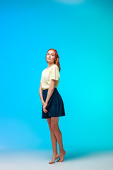 Red-haired girl in a short skirt stands on a blue-green background