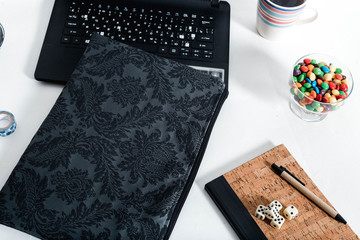 Black laptop on white desk with laptop case, candy, diary, clock