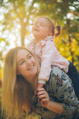 piggyback mother playing with daughter at autumn city park