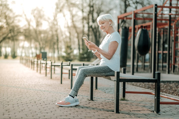 Cheerful elderly female person relaxing at the bench