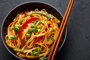 Vegetarian Schezwan Noodles or Vegetable Hakka Noodles or Chow Mein in black bowl at dark background. Schezwan Noodles is indo-chinese cuisine hot dish with udon noodles, vegetables and chilli sauce