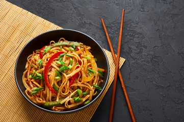 Vegetarian Schezwan Noodles or Vegetable Hakka Noodles or Chow Mein in black bowl at dark background. Indo-chinese cuisine hot dish with udon noodles, vegetables and chilli sauce. Copy space