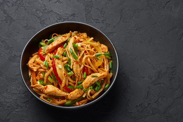 Chicken Schezwan Noodles or Hakka or Chow Mein in black bowl at dark background. Schezwan Noodles is indo-chinese cuisine hot dish with udon noodles, vegetables and chilli sauce. Copy space
