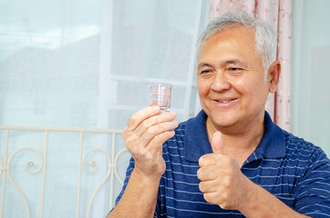age, medicine, health care and people concept - senior man looking at medicine in his hand and showing with thumb up to the side with happy face smiling at home or hospital office