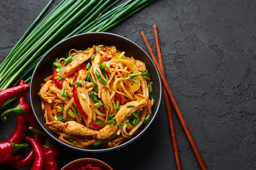 Chicken Schezwan Noodles or Hakka or Chow Mein in black bowl at dark background. Schezwan Noodles is indo-chinese cuisine hot dish with udon noodles, vegetables and chilli sauce. Copy space