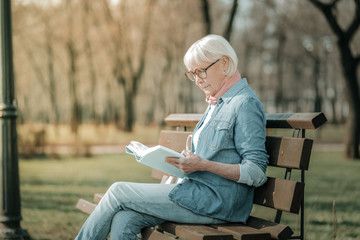 Prepossessing elderly madam in glasses reading intently a book