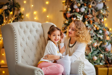 happy mom and daughter in a chair near the Golden Christmas tree