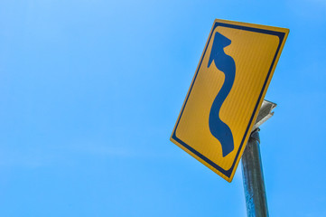 yellow road sign (winding road) on blue sky background