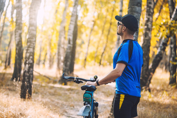 Fototapeta premium Happy bearded man cyclist rides in the sunny forest on a mountain bike. Adventure travel.