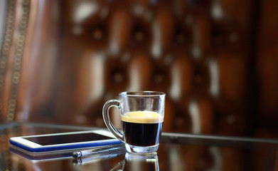 Cup of coffee with the phone on the glass table